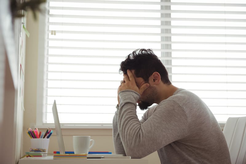 A man is sitting down rubbing his head because he's feeling a warm sensation come from there, possibly due to his high anxiety.