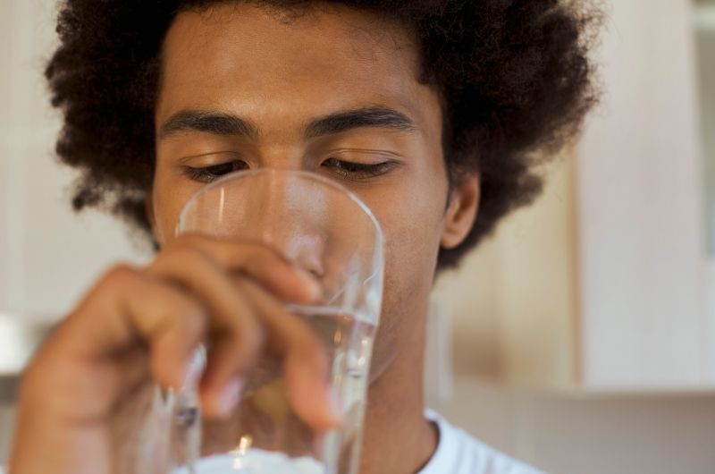 A young man is drinking plenty of water after having popcorn to avoid bloating that he's had before when eating popcorn.