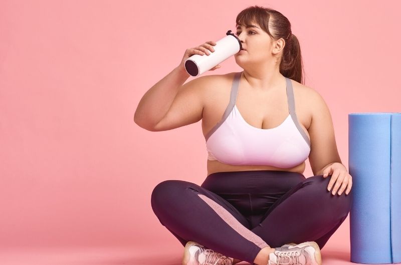 A young woman is sitting down drinking water after her rigorous exercise