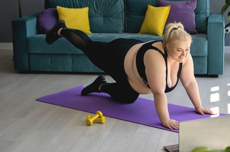 A young woman who is obese is working out at home to lose weight and get fit