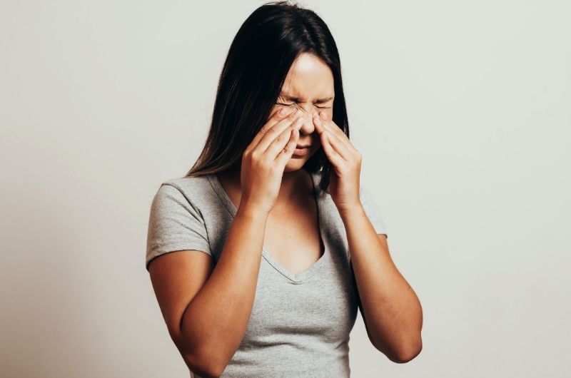 A woman is touching her sinus area as she's experiencing pain after doing a sinus rinse