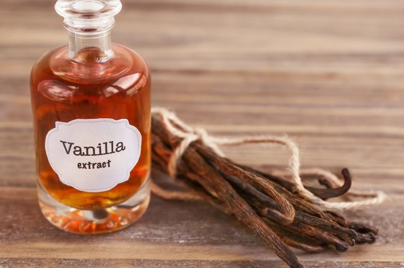A small bottle of vanilla extract next to some tied up raw vanilla beans