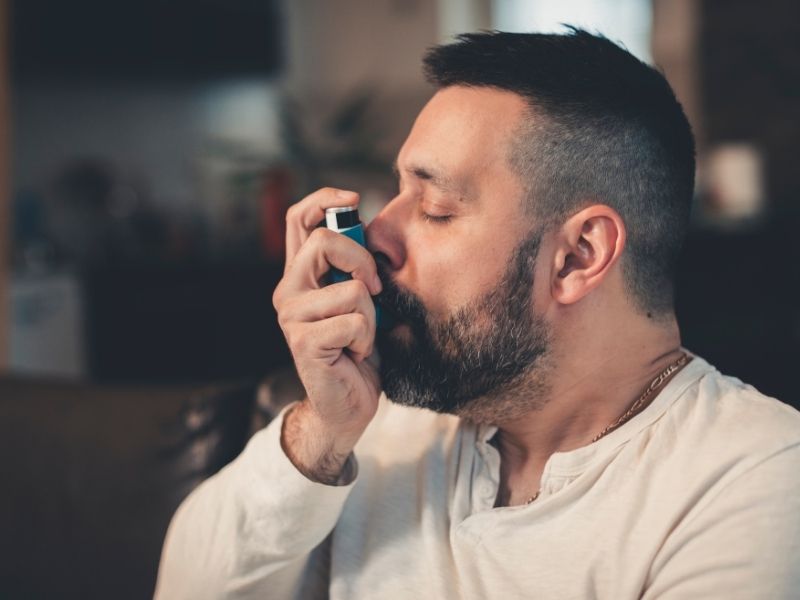 A man is using his inhaler to help with his breathing condition