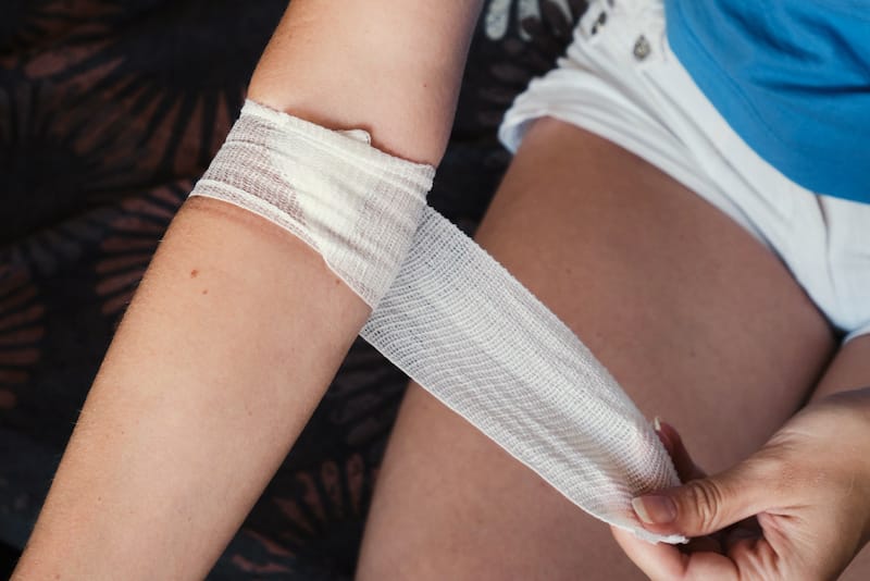 A woman is trying to remove a bandage that is stuck to her wound on her arm