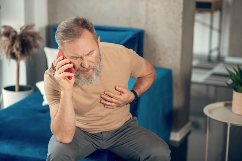 An older man is sitting down after feeling irregular and fast heartbeats and is now calling his doctor
