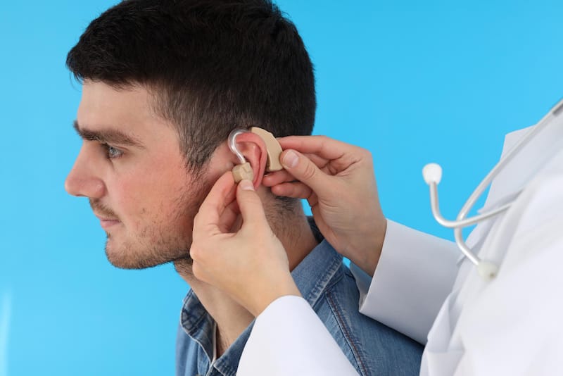An Otolaryngologist is helping place new hearing aid pieces in his patients ears