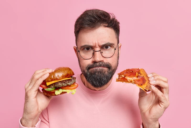 A man holding a burger and pizza, foods that can affect his urine smell later on