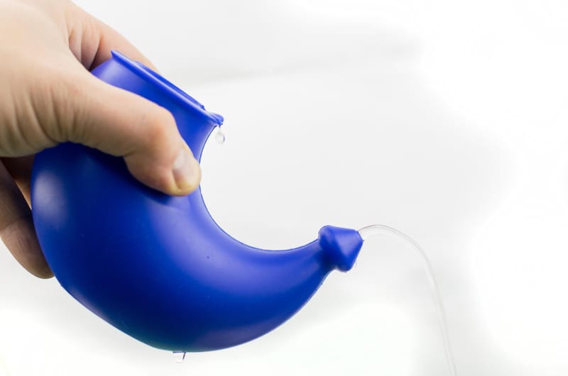 A person is using a neti pot and tilting it to show how the water flows out