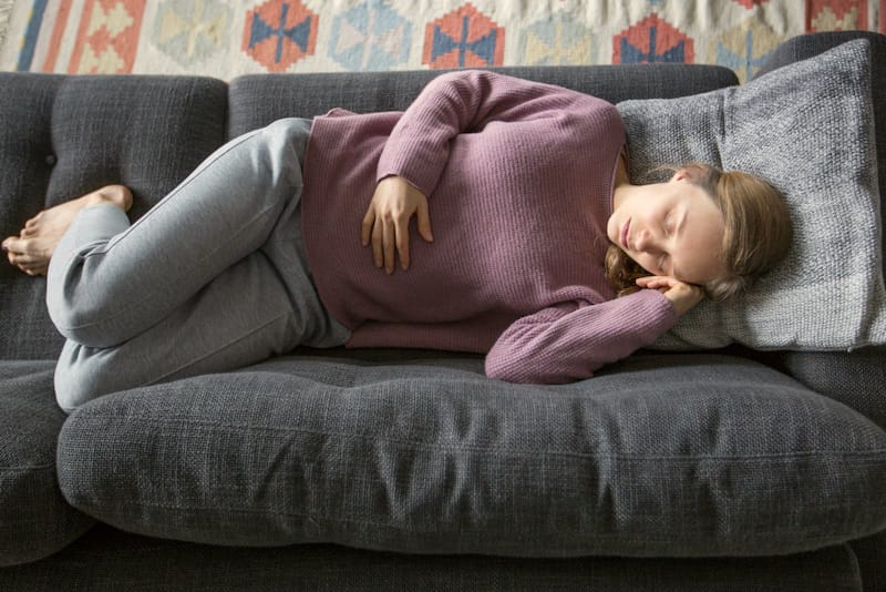 A woman is laying on the sofa trying to comfort herself after getting food poisoning recently