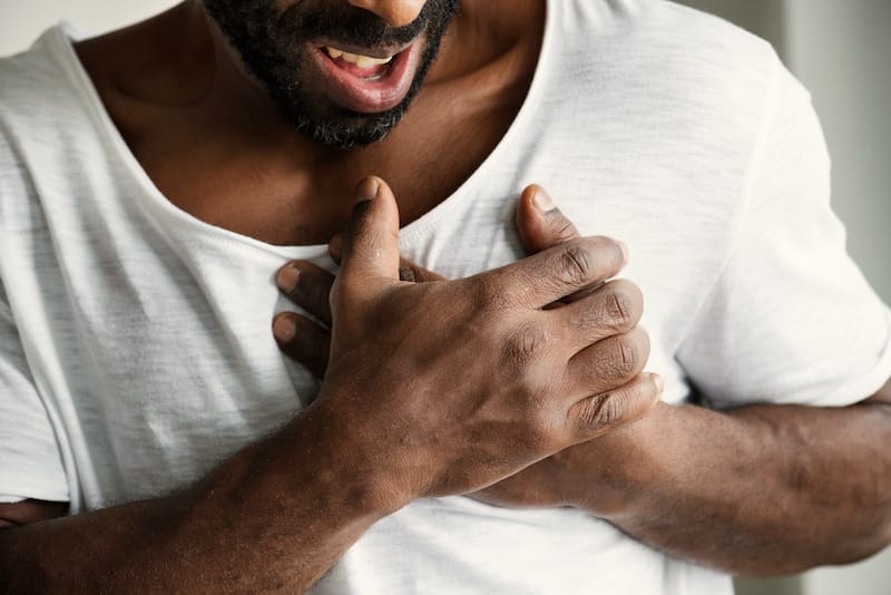 A man is clenching both his hands on the left side of his chest as if he might be having a heart attack.