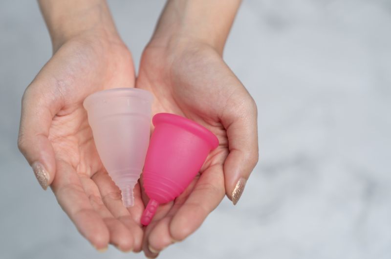 A woman holding 2 different colored menstrual cups to be used during her period
