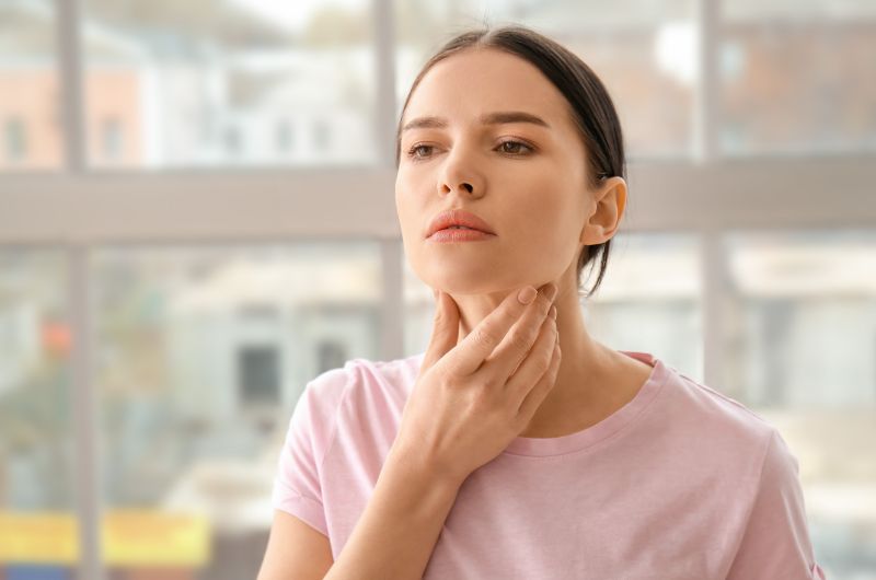 A woman is touching her throat as she's feeling discomfort from the area where her thyroid is
