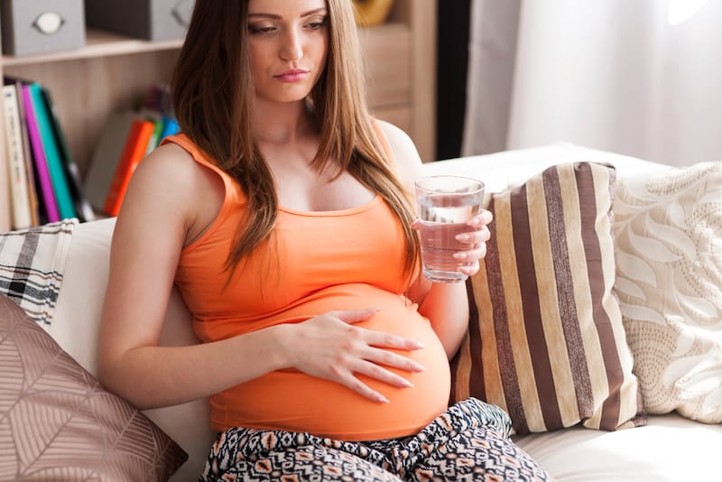 A pregnant woman is resting and drinking water to help her feel better after having food poisoning as a result of eating raw seafood.