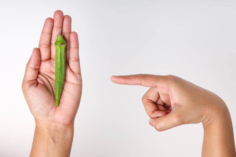 A person holding a small okra in their hand as an example of a small penis