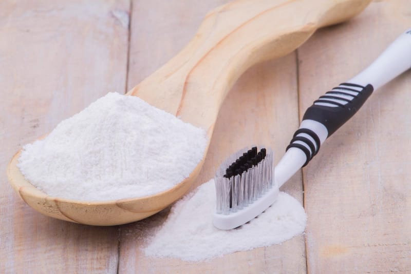 A large spoon of baking soda is shown next to a brush, to be used on one's teeth to whiten the teeth.