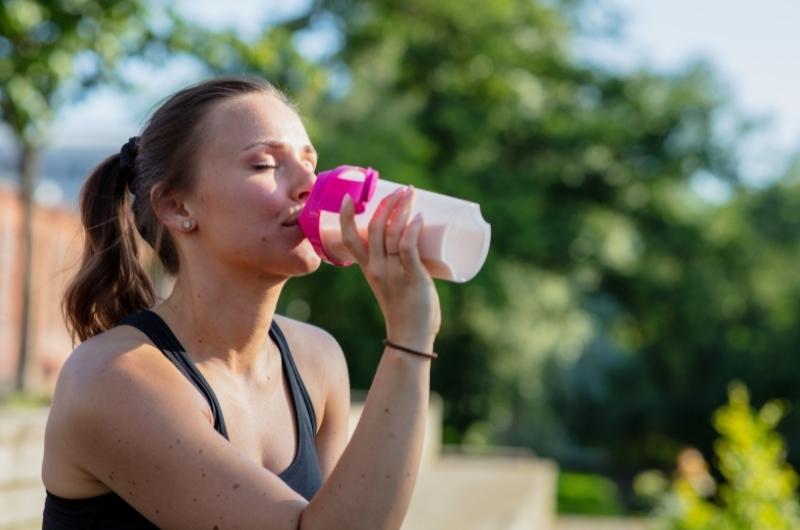 A pregnant woman is drinking a protein shake after her outdoor workout