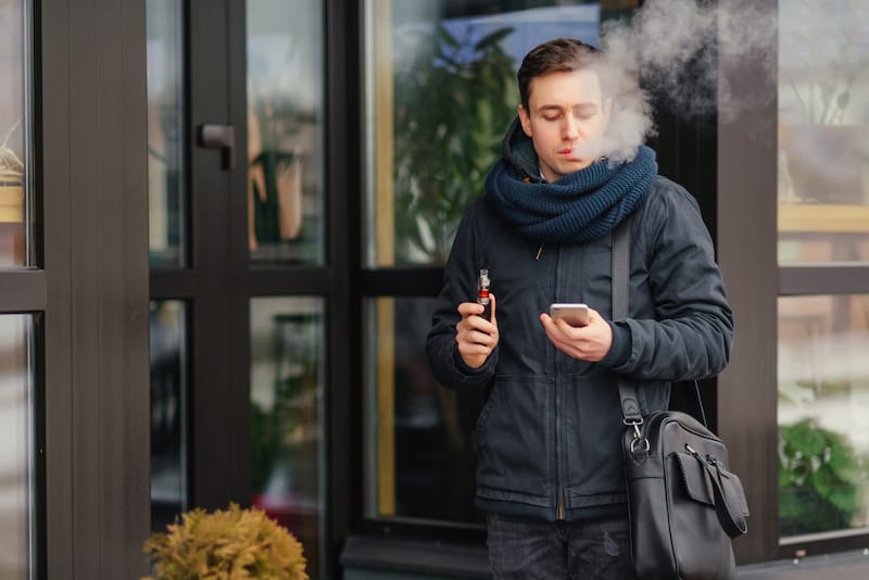 A man is vaping outside with a cartridge that does not have nicotine