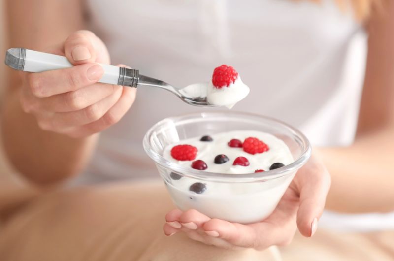 A pregnant woman is eating yogurt with some strawberries and blueberries