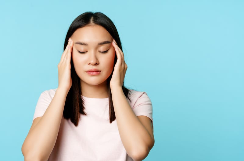 A young woman is closing her eyes and rubbing her temples as she is feeling anxiety