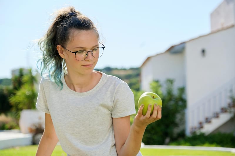 A young woman is eating a green apple to make sure she's eating enough daily fiber for healthy bowel movements