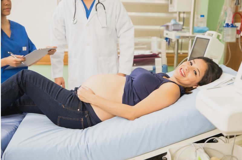 A pregnant woman is happy and excited as she is laying down in a hospital bed getting ready to have her baby