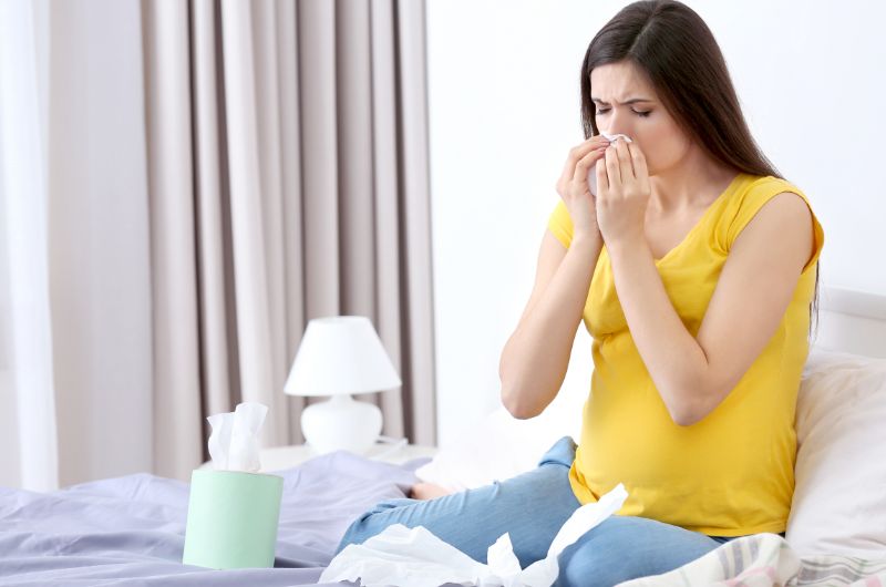A young woman is blowing her nose because of her allergies, which might be the cause of her postpartum hives.