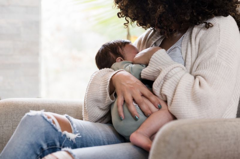 A mom is sitting down and breastfeeding her newborn baby