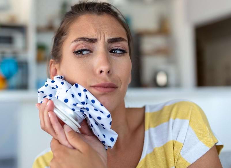 A young woman is trying to reduce her jaw swelling with an ice pack after receiving oral surgery
