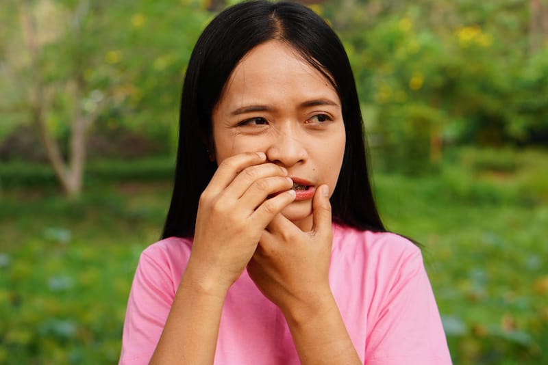 A woman is clenching her mouth as the roof of her mouth has a painful bump