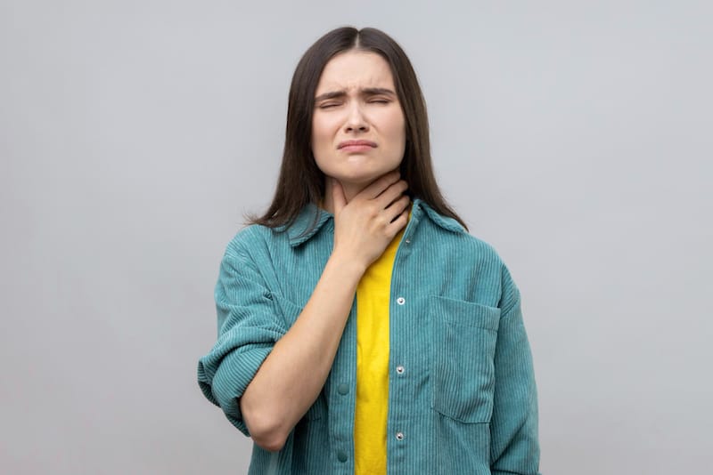 A woman is clenching her throat because she's feeling pain from her thyroid area
