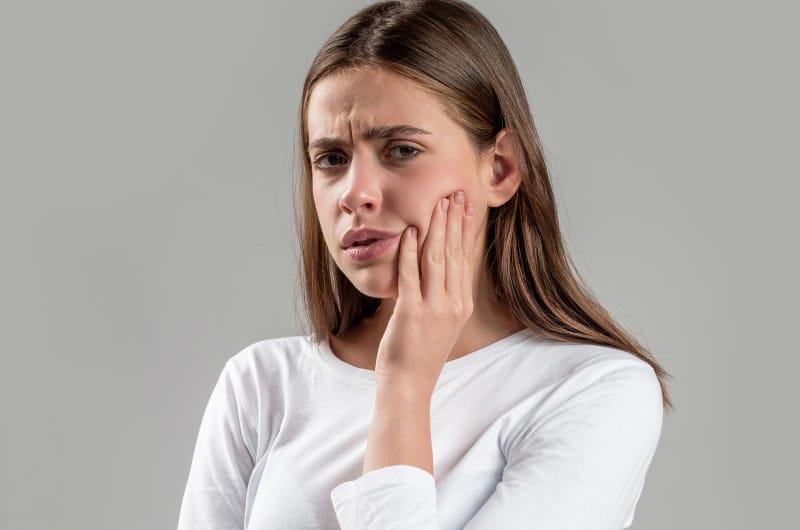 A young woman is clenching the left side of her jaw as she has an infection and is in pain