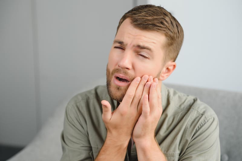A man is touching one side of his jaw that's causing him pain after he just yawned