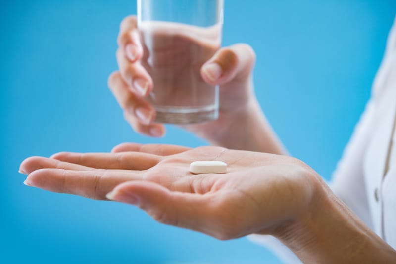 A woman is holding out her medicine that she's about to take with a glass of water