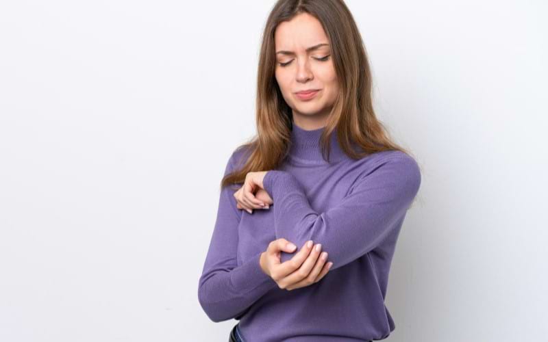 A woman with arthritis is holding her left elbow in noticeable pain; she might have high levels of d-dimer.