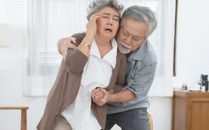 An old man is holding his wife, who feels dizzy and might be getting a stroke.