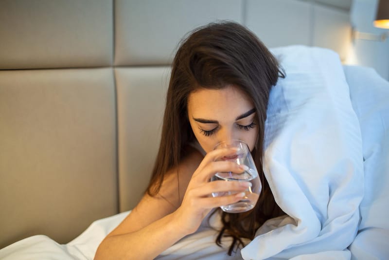 A woman took her prescription sleeping pills and is drinking water before going to sleep