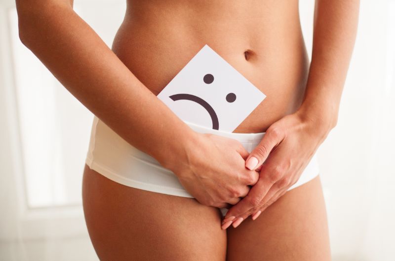 A woman is holding a sad-face card near her vagina to signify that she has a yeast infection