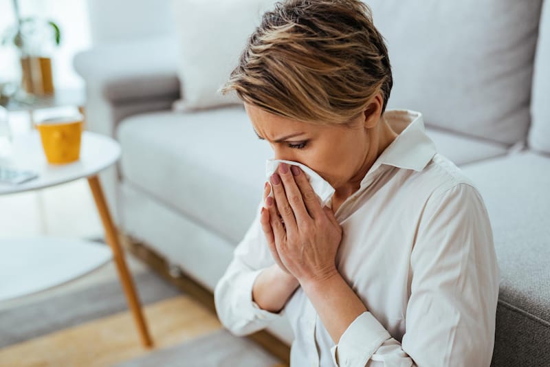 A woman with allergies is blowing her nose after sneezing a few times.