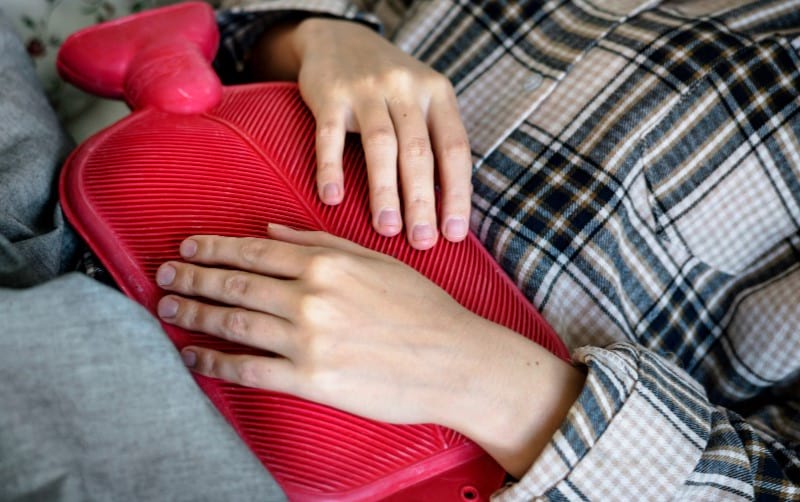 A woman is using a hot water bag in bed to reduce her pain and swelling from genital herpes.