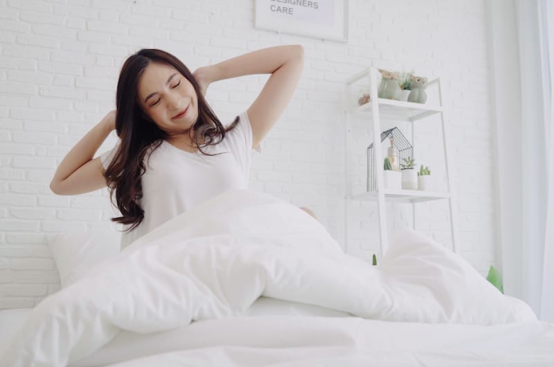 A woman is stretching in her bed after just waking up from her sleep