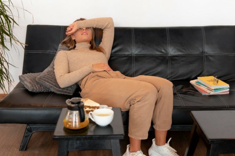 A young woman experiencing pain in her stomach lying on the couch after drinking coffee. 