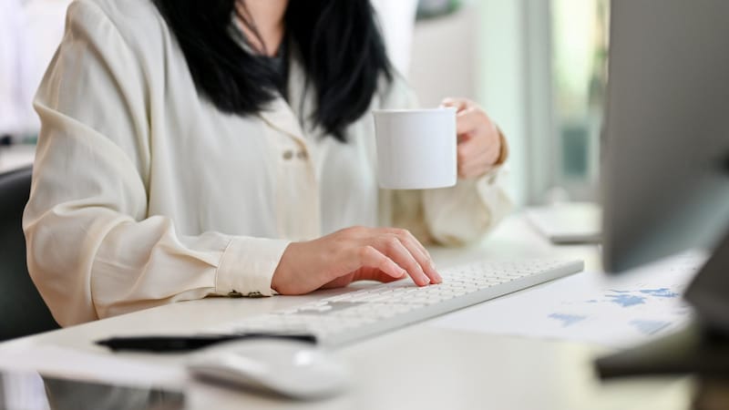 A woman is drinking decaffeinated coffee while she works to prevent her IBS symptoms.