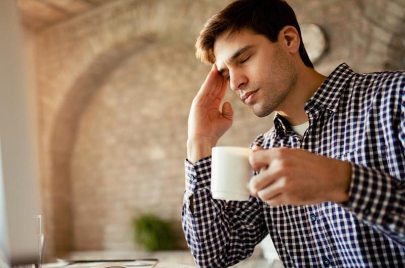 Young man is holding his head while drinking coffee during brain injury recovery