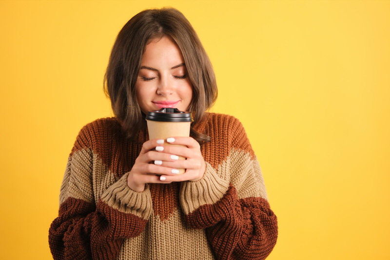 A young woman is smiling with her eyes closed as she takes enjoys the aroma of her coffee