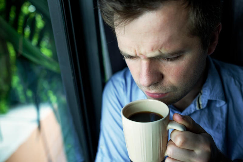 A man looks groggy and somewhat unhappy as he is having his morning coffee to wake up
