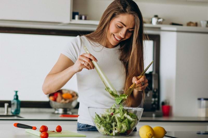 Young woman is making salad in her kitchen which is a great way to recover from brain injury.