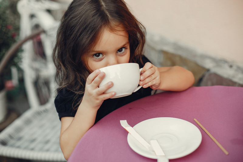 A young girl is drinking a little bit of her parents cappuccino from a cup