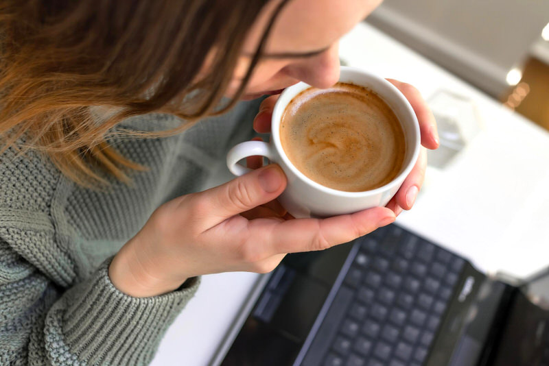 A woman drinking a cappuccino while working on her laptop