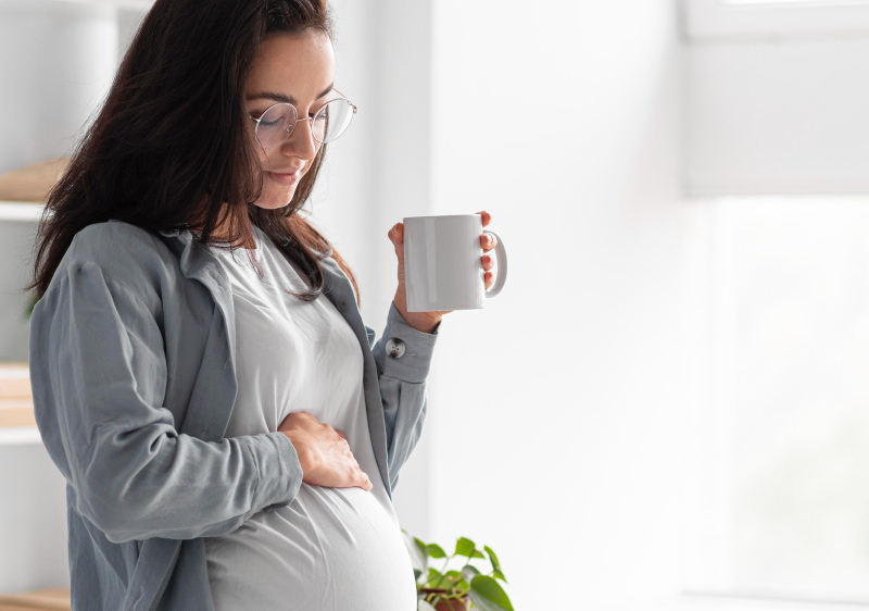 A pregnant woman is drinking coffee and looking at her growing belly
