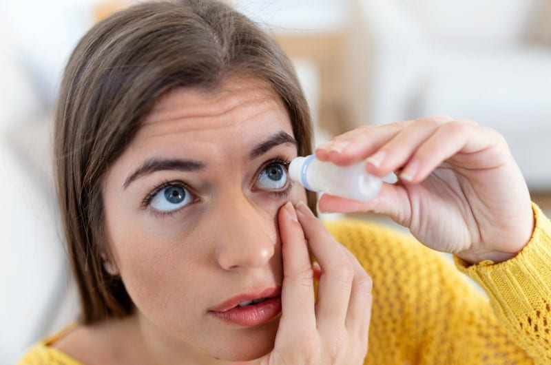 A woman is putting eye drops in her eyes to avoid getting dry eyes.